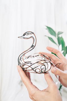 a person holding a metal swan sculpture in their hands, with a plant behind it