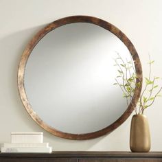 a round mirror sitting on top of a dresser next to a vase with a plant in it