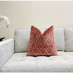 a white couch with a red pillow on top of it next to a flower vase