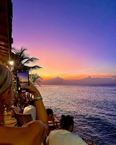 a woman taking a photo with her cell phone on the deck of a restaurant overlooking the ocean