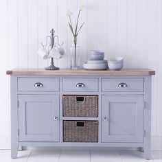 a blue sideboard with wicker baskets on top and flowers in vases next to it