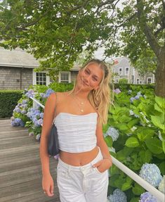 a young woman standing on a porch next to blue hydranges and trees in the background