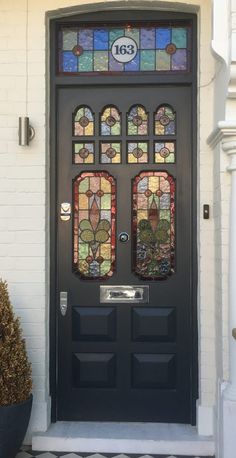 a black front door with stained glass windows on the top and bottom panel, along with a potted plant