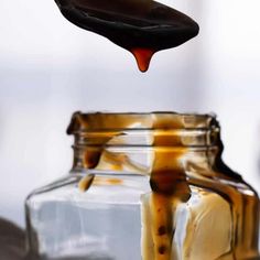 a spoon pouring caramel syrup into a glass jar