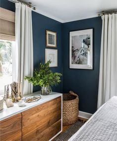 a bedroom with blue walls and white drapes on the windowsill, a large wooden dresser