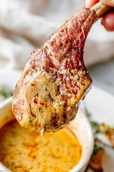 a hand holding up a piece of meat over a bowl of soup