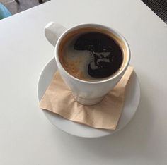 a cup of coffee sitting on top of a white saucer next to a napkin