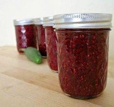 three jars filled with raspberry jam sitting on top of a wooden table next to a green pepper