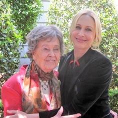 two women standing next to each other in front of some bushes and trees with their hands out