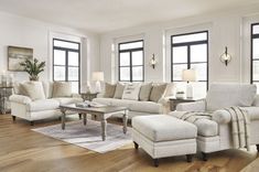 a living room filled with white furniture and lots of windows on the side of it