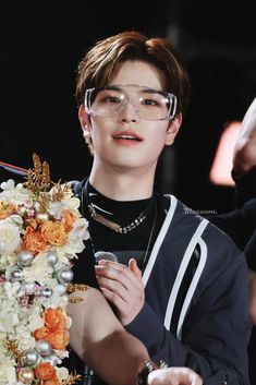 the young man is wearing glasses and holding flowers in his hand while standing next to a microphone