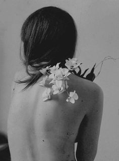 the back of a woman's body with flowers on her shoulder and chest, in black and white