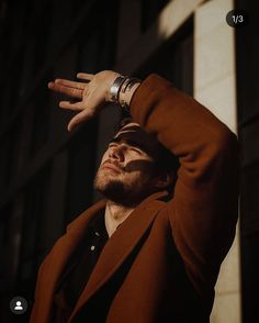 a man in a brown jacket is holding his hand up above his head and looking off into the distance