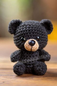 a small black crocheted teddy bear sitting on top of a wooden table with eyes wide open