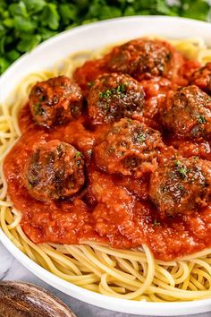 spaghetti with meatballs and tomato sauce in a white bowl on a marble countertop