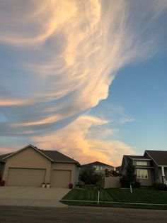 some clouds are in the sky over houses and lawns on a sunny day at dusk