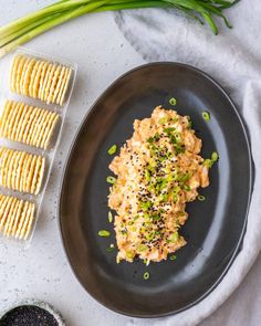 a black plate topped with food next to some crackers and green onion wedges