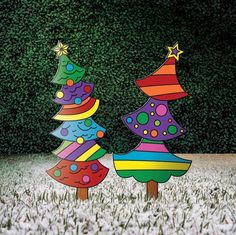 three brightly colored christmas trees are standing in the middle of a field with snow on the ground