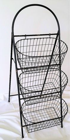 a three tiered metal basket holder on a white sheet covered floor with the bottom section folded down