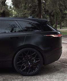 the black range rover is parked in front of some trees