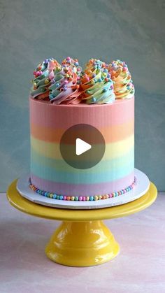 a rainbow cake with frosting and sprinkles is on a yellow stand