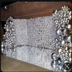 an artistic sculpture made out of silver balls and metal pans on a wall in front of a brick building