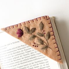 an embroidered piece of cloth with leaves on it sitting on top of a book page