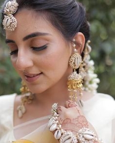 a woman in a white sari with gold jewelry on her head and hands, looking at the camera