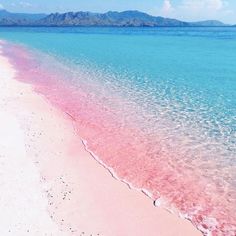 the beach is pink and blue with white sand on it's shore, as well as mountains in the distance