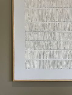 a white painting hanging on the wall next to a brown framed piece of art that has lines drawn across it