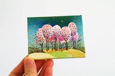 a hand holding up a small card with trees painted on it