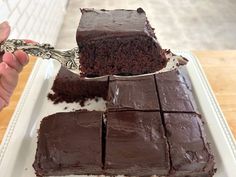 a person holding a knife over a piece of chocolate cake on a white platter