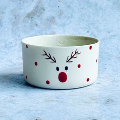 a white bowl with red and black polka dots on the rim has a reindeer's face painted on it