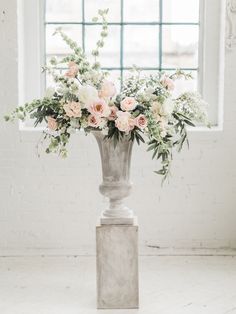 a vase filled with white and pink flowers next to a window in an empty room