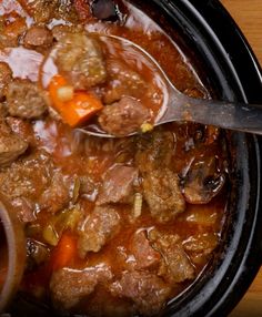 a spoon full of meat and vegetables in a slow cooker