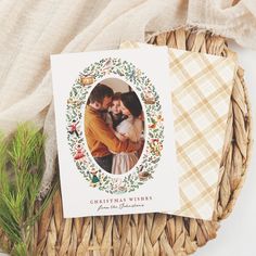 a christmas card sitting on top of a wicker basket next to a pine branch