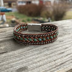 a brown leather bracelet with turquoise beads on top of a wooden table in front of a house