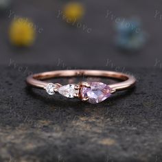 a pink and white diamond ring sitting on top of a black stone surface with yellow flowers in the background