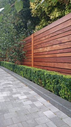 a wooden fence next to a sidewalk and some bushes on the side of a building