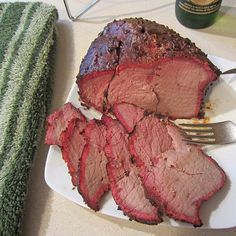 a piece of meat on a white plate with a fork and towel next to it