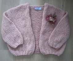 a pink knitted sweater with flowers on the front and back, sitting on top of a wooden floor