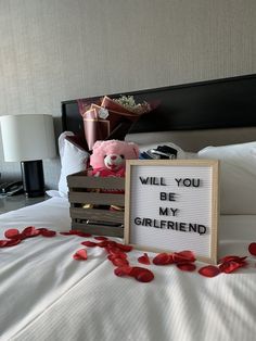 a sign that says will you be my girlfriend next to a teddy bear on a bed