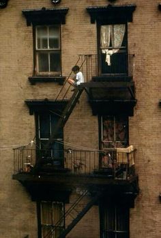 a man standing on top of a fire escape in front of a tall brick building