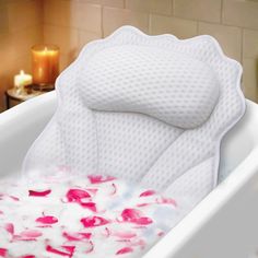 a bathtub filled with pink and white flowers next to a candle on a table