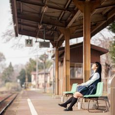 a woman sitting on a bench in front of a train station