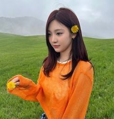 a girl in an orange shirt is holding a yellow flower and posing for the camera