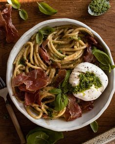 a white bowl filled with pasta, meat and pesto on top of a wooden table