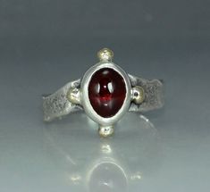 The ring is made in recycled silver and  has been textured and a patina was applied. The ring is made in heavy gauge silver and will last a lifetime. The stone is a garnet of very high quality with great color. color. Any stone in any size or shape can be used. The garnet is 13mm x 6mm. Four 14k gold orbs are added to the sides of the setting. This ring is one of a kind.   The ring can be ordered in any size wanted. I offer 1 free resize as we can't meet and try on ring gauges for a perfect fit. I offer these rings in 14K and 18K yellow gold, ask about prices! Silver Ruby Ring, Garnet Ring Silver, Rustic Ring, Garnet Engagement Ring, Rustic Rings, Organic Rings, Cabochon Ring, Silver Work, Uncut Diamond