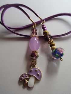 a close up of a necklace with beads and charms on a purple cord, sitting on a white surface