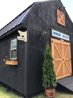 a black barn with a sign that says farm on the side and potted plants in front